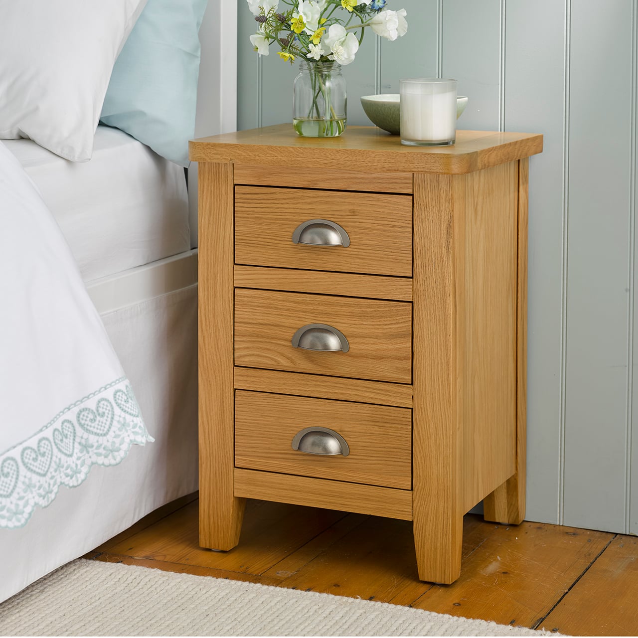 Wooden bedside table with three drawers and a vase on top