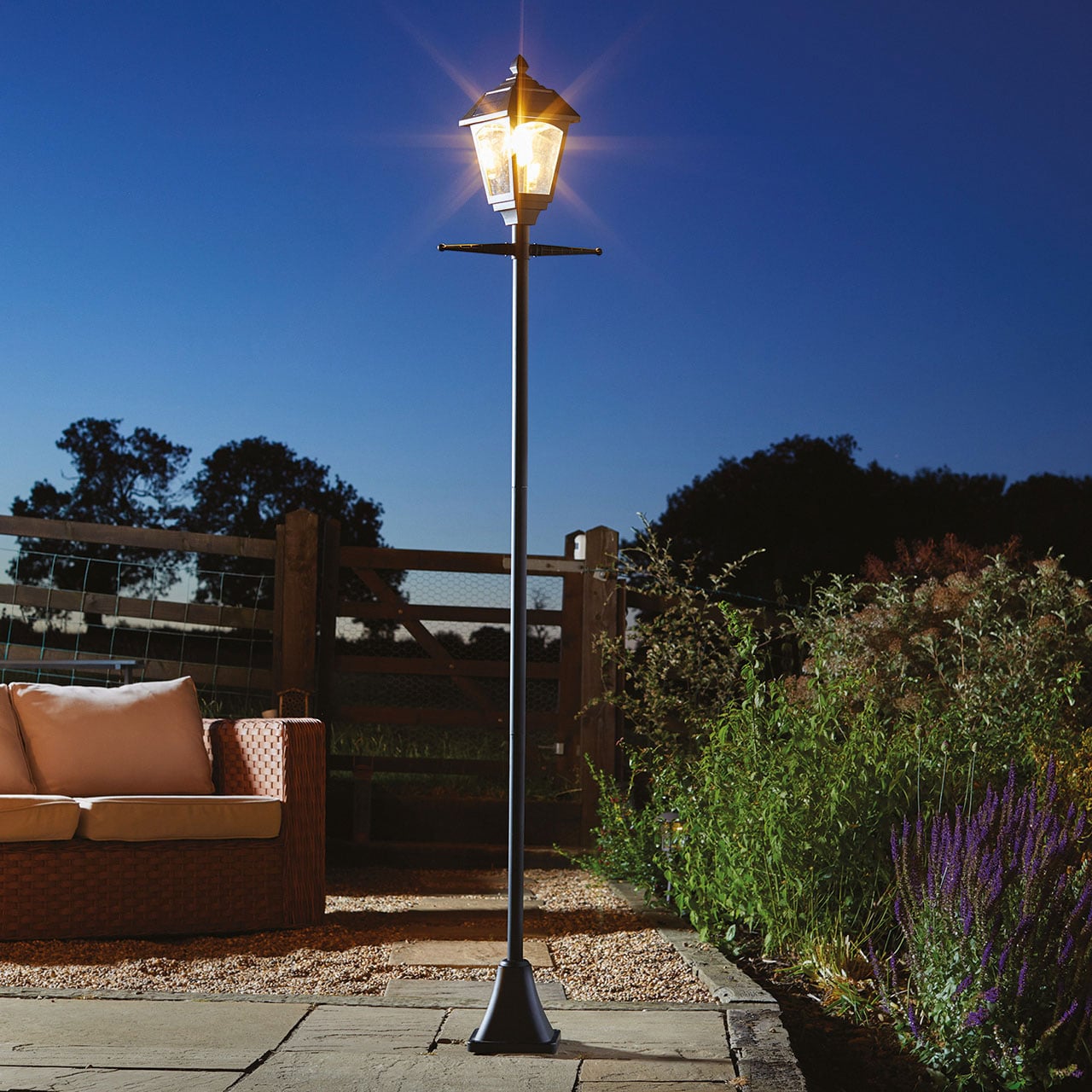 Tall solar lamp post with warm light in a garden setting