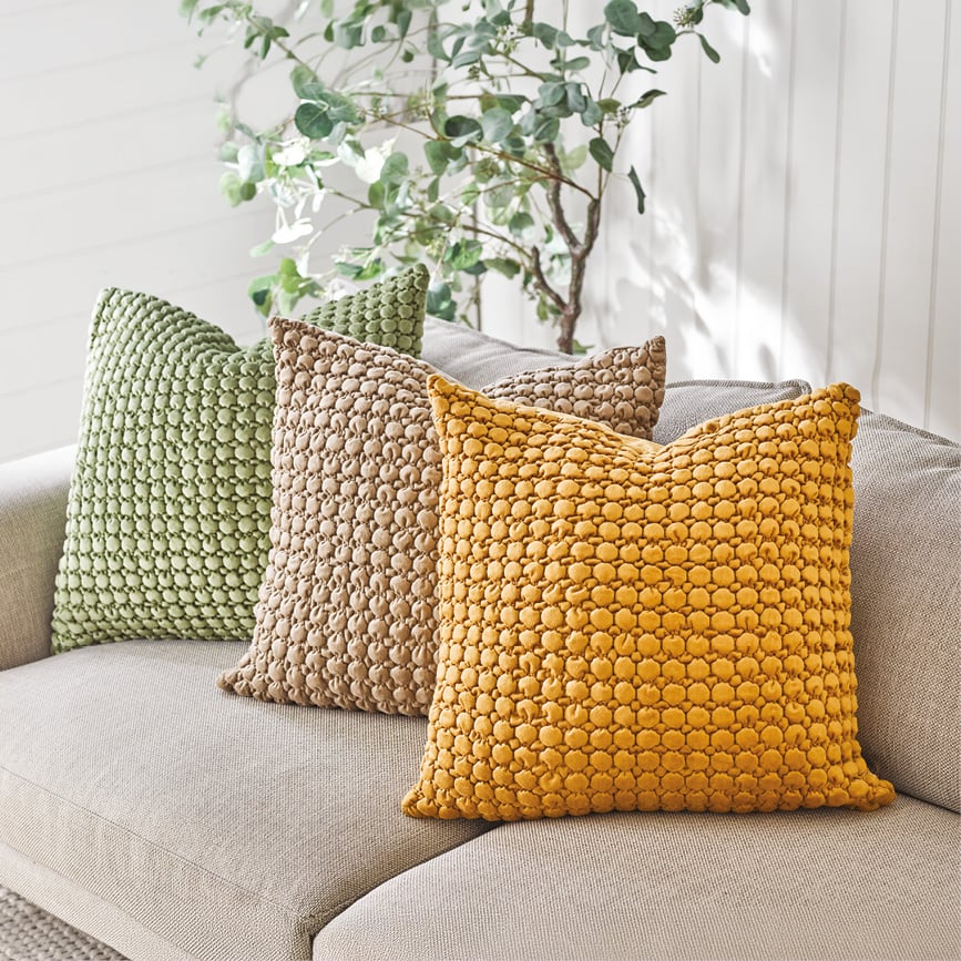 Three textured cushions in green, brown, and mustard yellow on a sofa