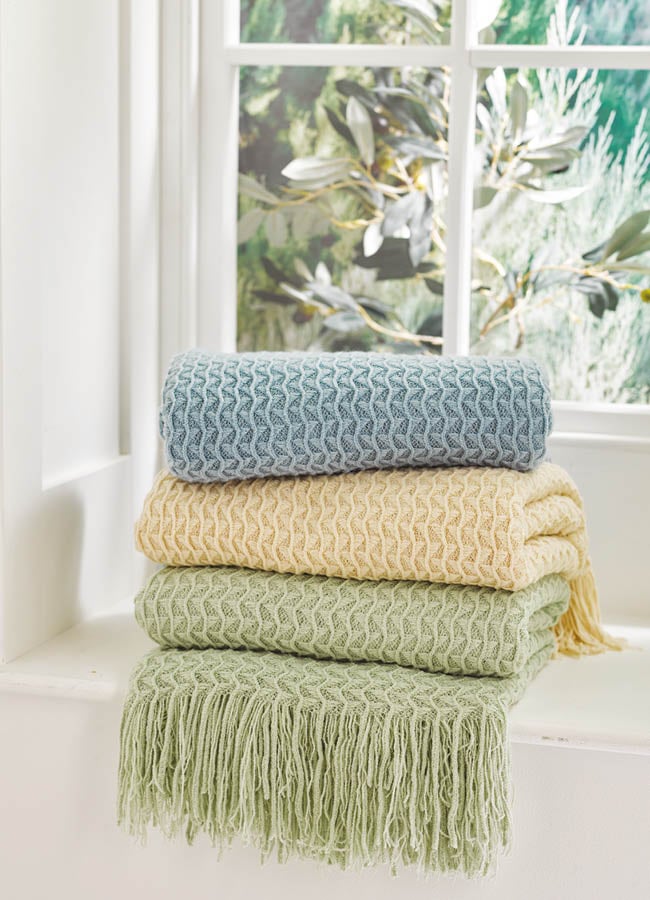 Image showing stack of coloured knitted throws in blue, natural and green