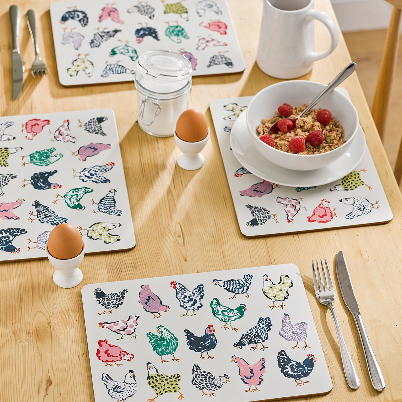 Ceramic chicken‑pattern placemats and coasters arranged on a wooden table.