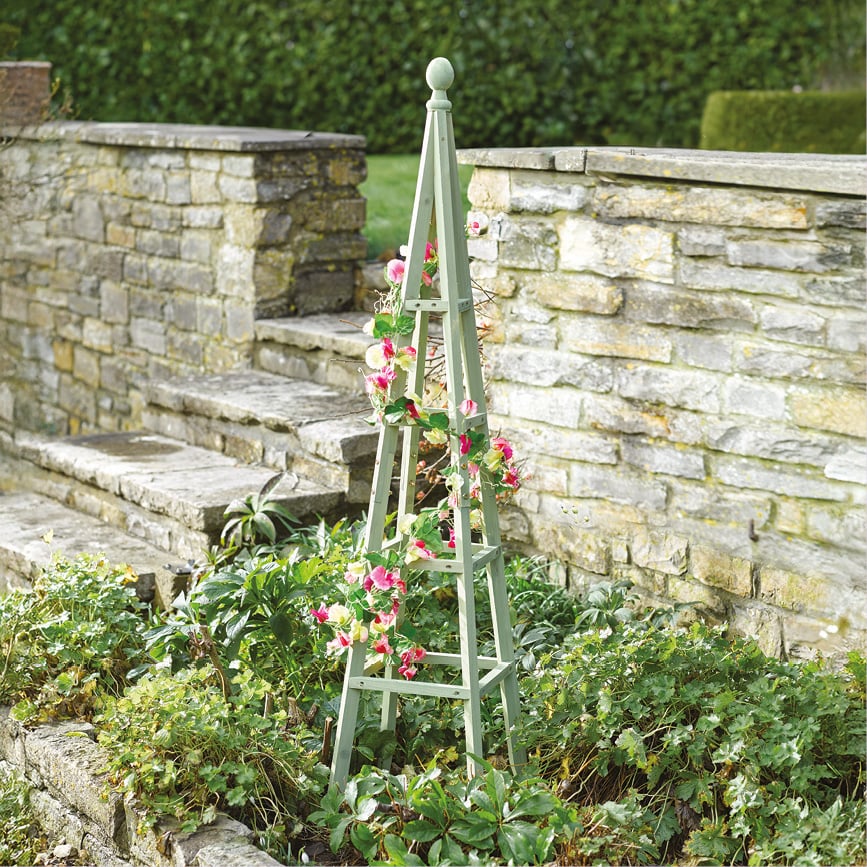 Sage green wooden obelisk in flowerbed